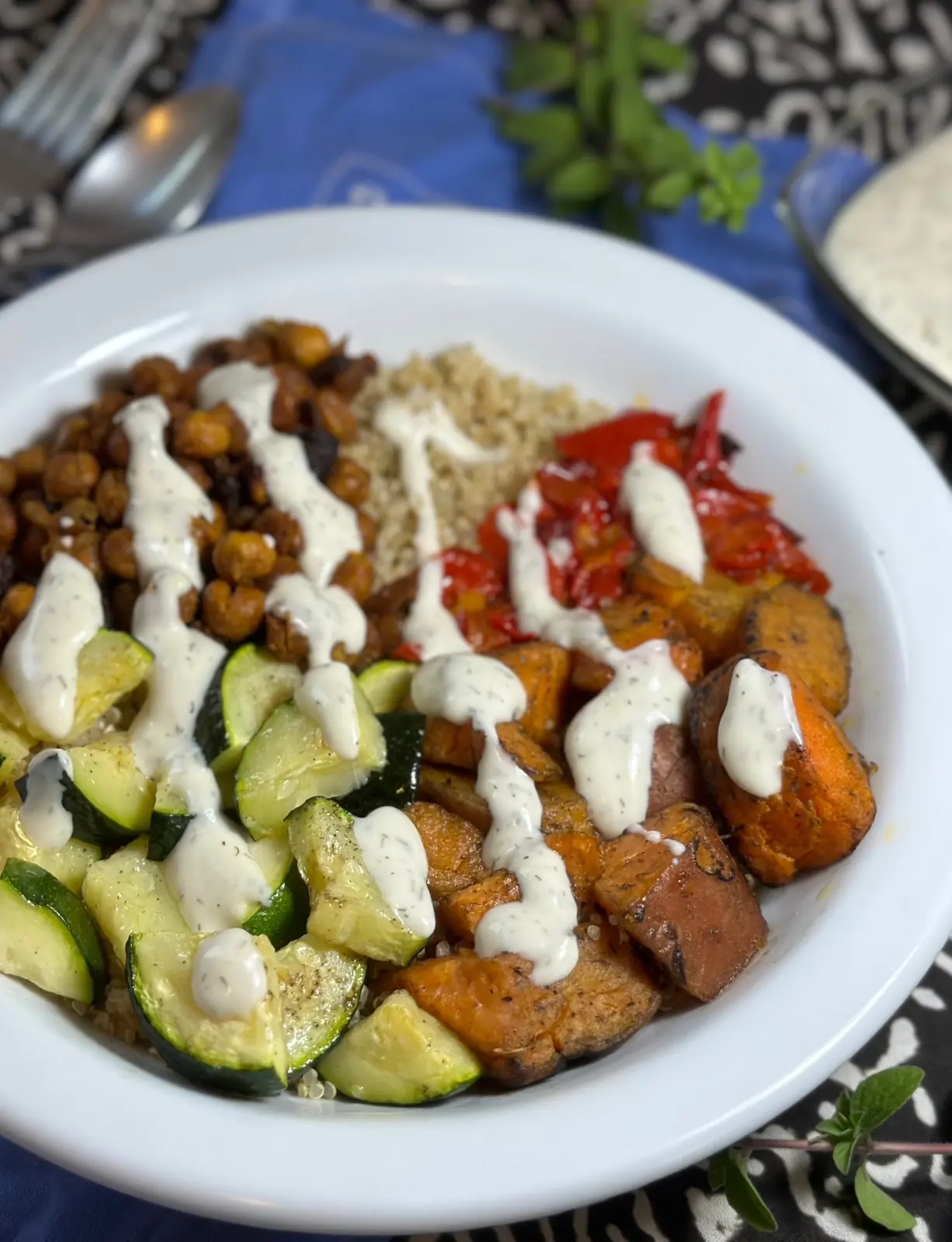 sweet potato chickpea buddha bowl with sweet potato, chickpeas, red pepper, quinoa and zucchini in a white bowl with lemon yogurt dressing drizzled on top