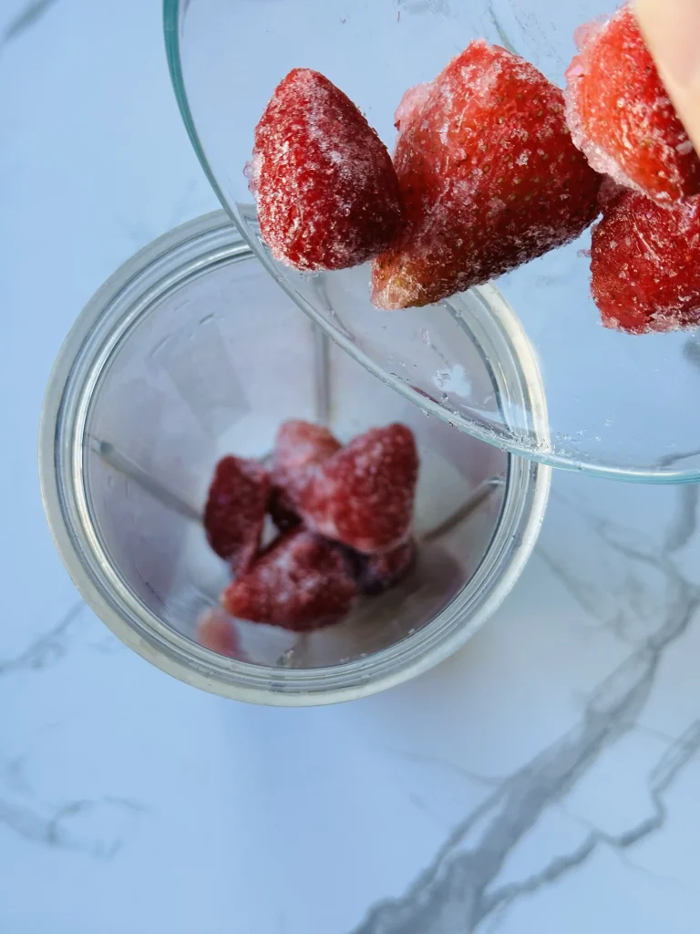 pouring frozen strawberries into a blender to make vitamin c smoothie