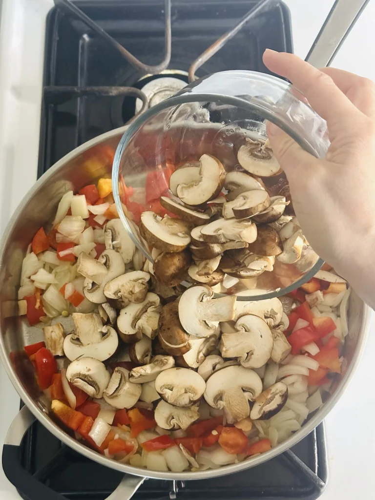 adding mushrooms to onions and peppers in a pan for meat sauce with mushrooms