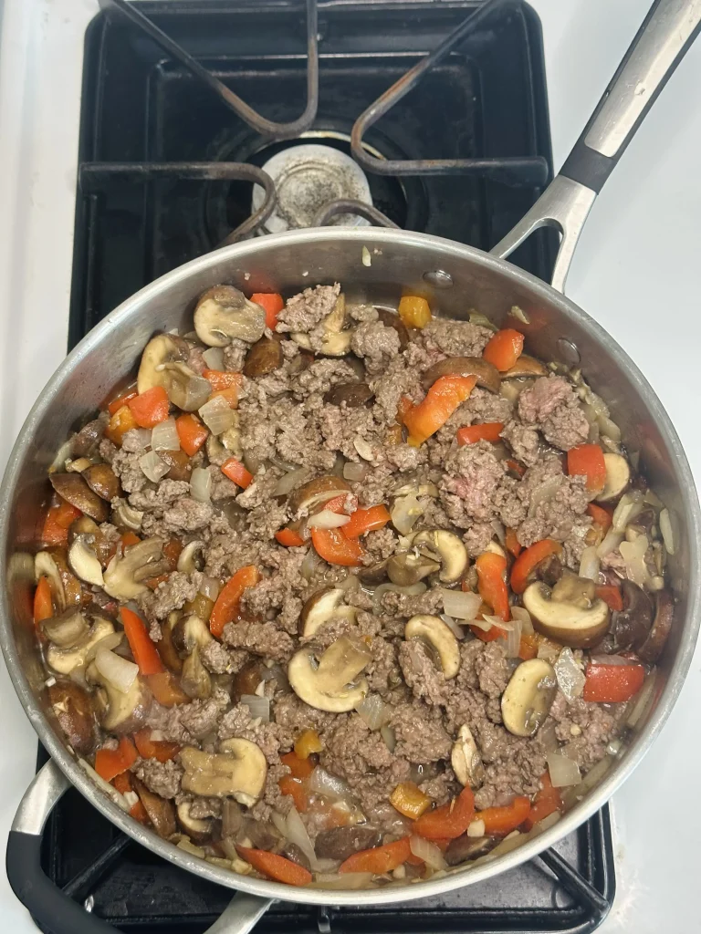 browning the meat with veggies in a pan for meat sauce with mushrooms