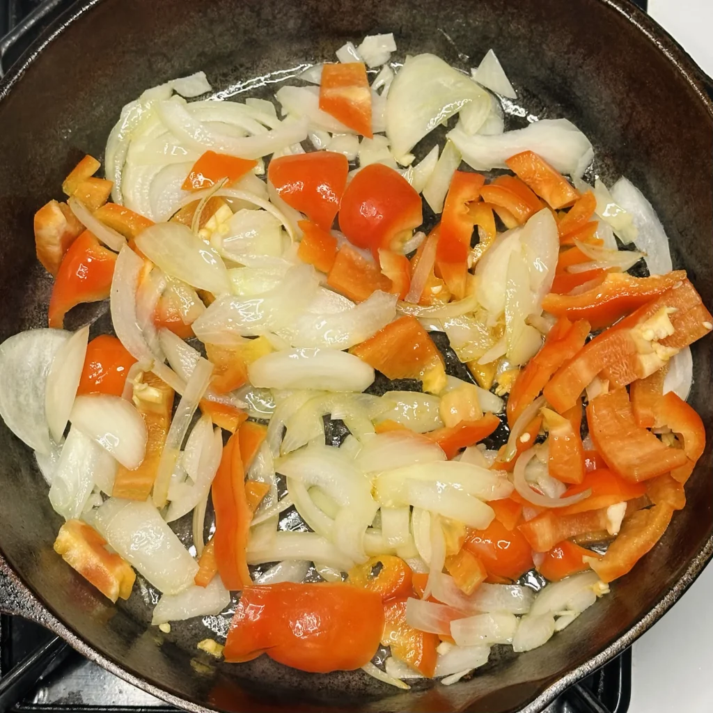 onion and red bell pepper cooking in a cast iron pot