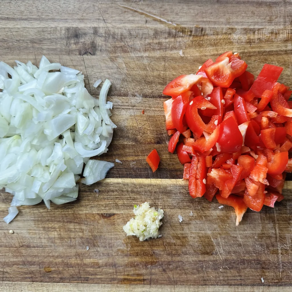 a wooden cutting board up close with chopped onion, bell pepper and garlic on it for black bean chili with corn