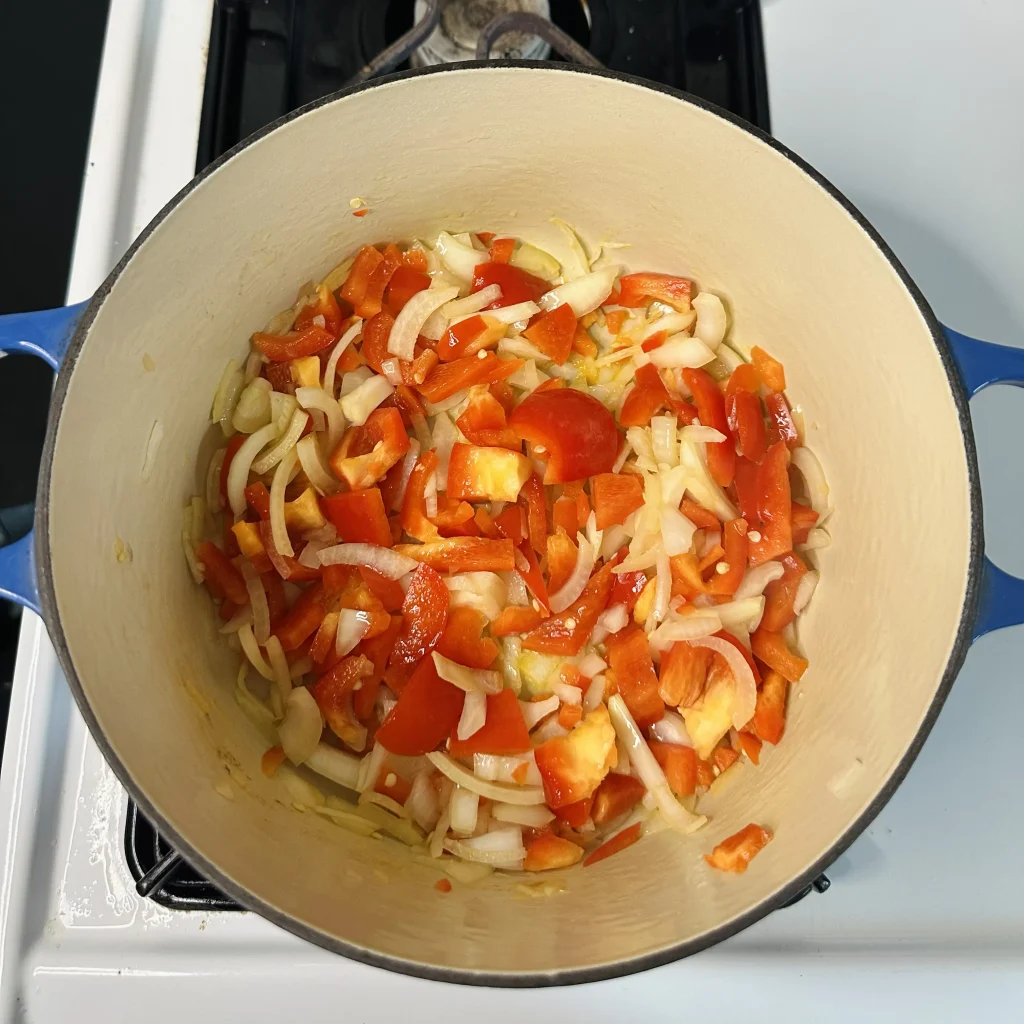 sauteeing onion and red bell pepper for black bean chili with corn in a cast iron pot on a white oven