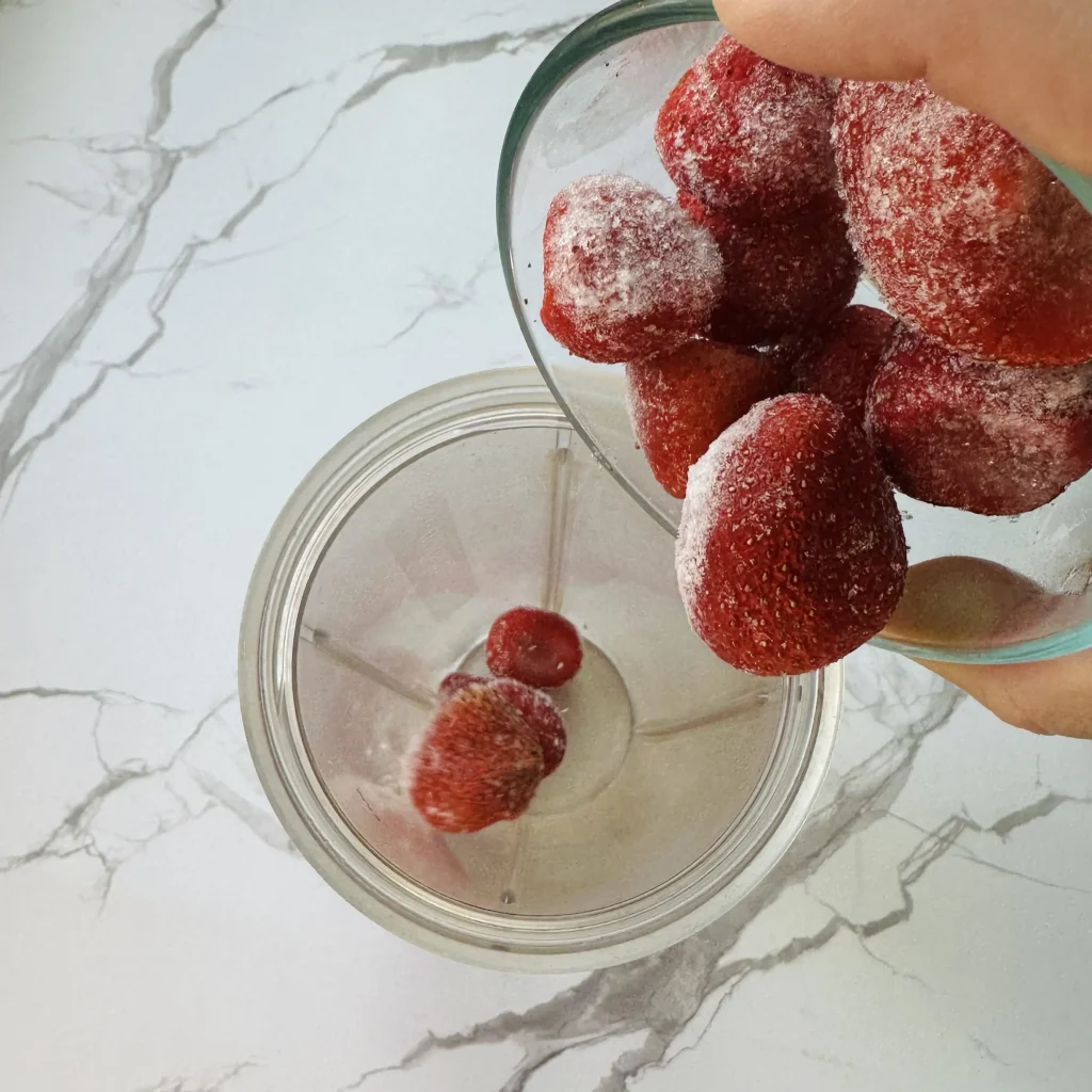 pouring frozen strawberries into a blender to make strawberry banana peanut butter smoothie