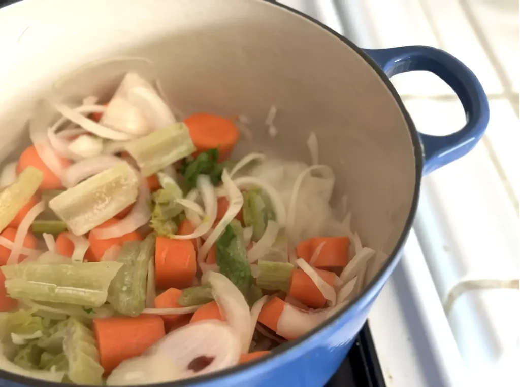 raw veggies like carrots, onion and celery in a blue pot