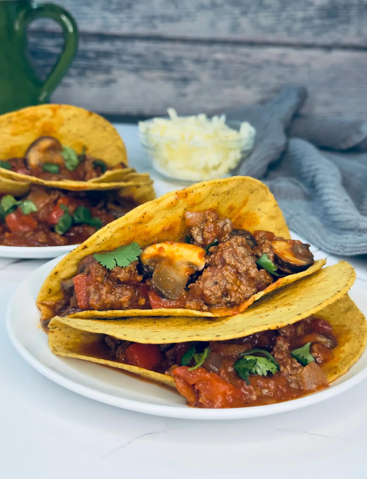 meat sauce with mushrooms stuffed into crunchy yellow tacos with a glass bowl of cheese in the background