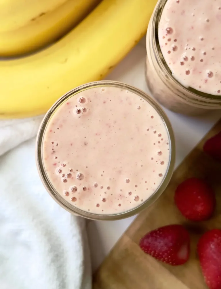 strawberry banana peanut butter smoothie feature image of a bird's eye view of a light pink smoothie slightly bubbling with bananas and strawberries in the background