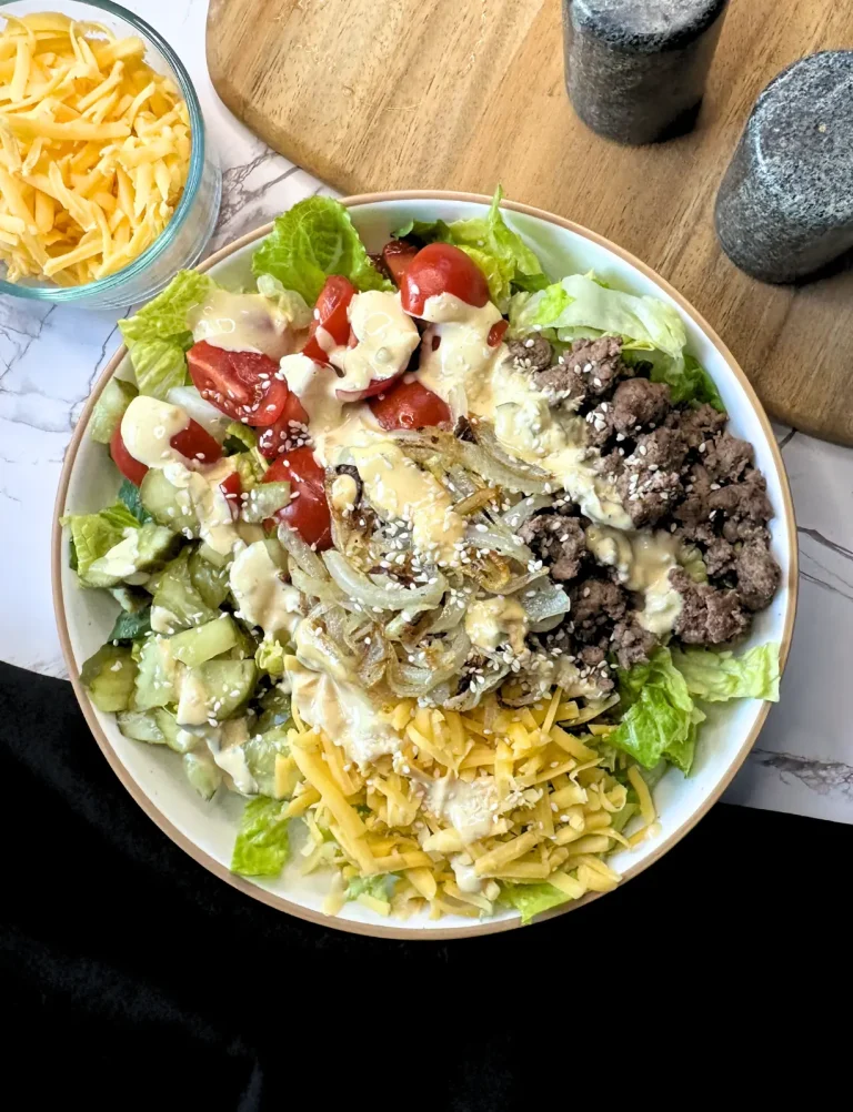 big mac salad in a white bowl with a black napkin, salt and pepper and a cutting board in the background
