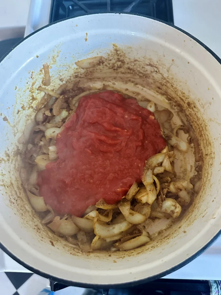 adding crushed tomatoes to curry in pot