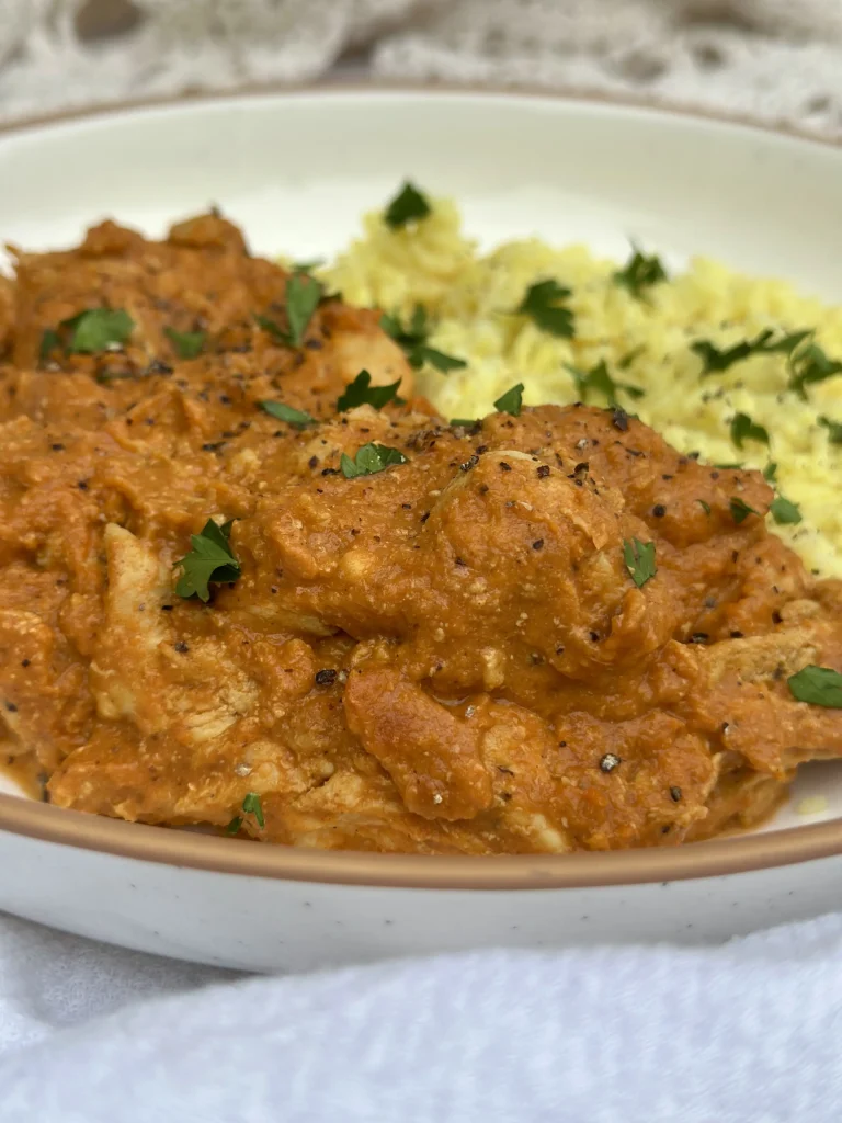 up close butter chicken on a plate with yellow rice