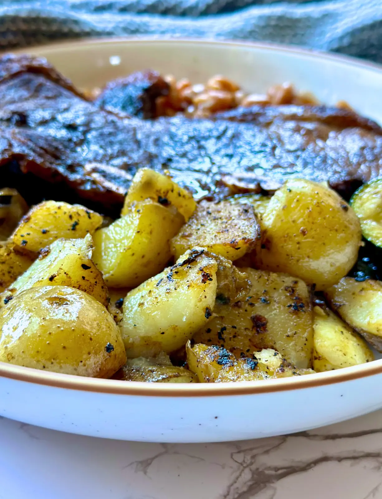 up close image of grilled home fries on a plate with steak and beans in the background