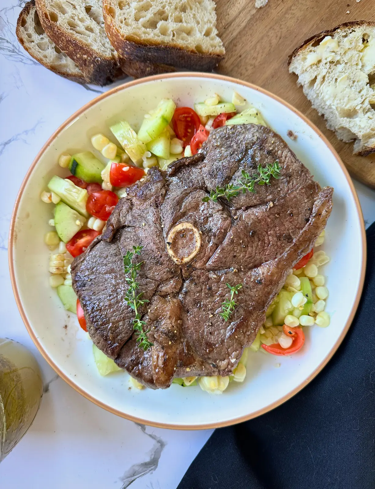 feature image of lamb chops on the grill sitting on a plate on top of a corn salad with bread in the background