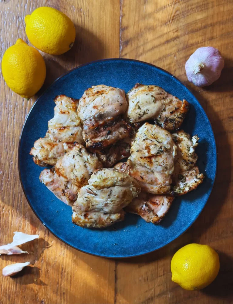 lemon and garlic grilled chicken on a blue plate with lemon and garlic in the background